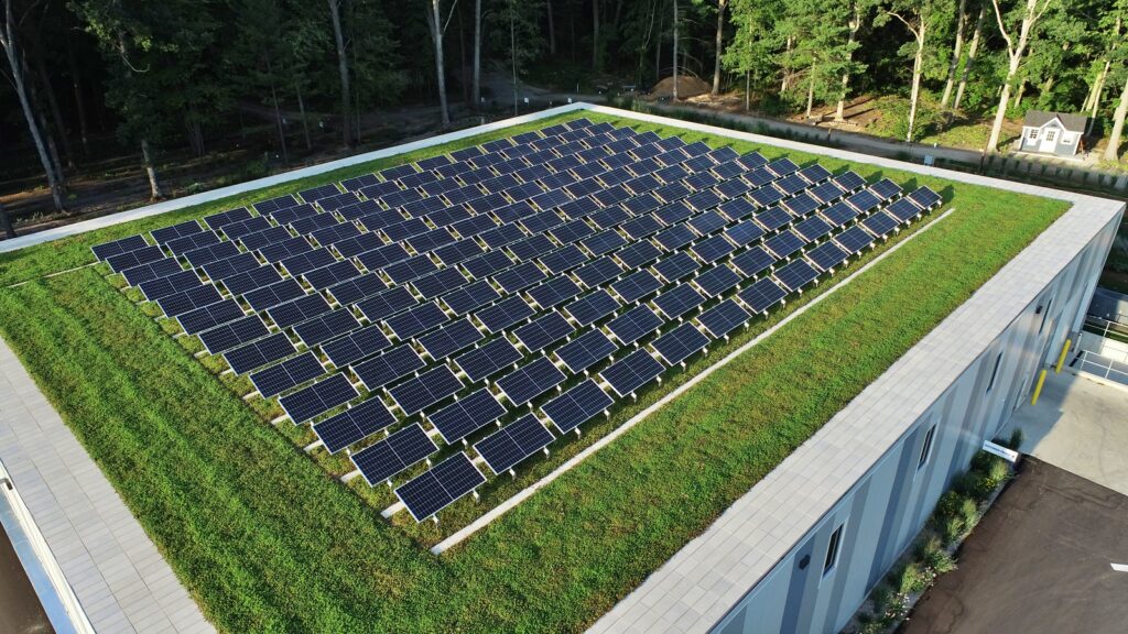 Flat building roof with green roof covering most of it and solar racks covering much of the green roof