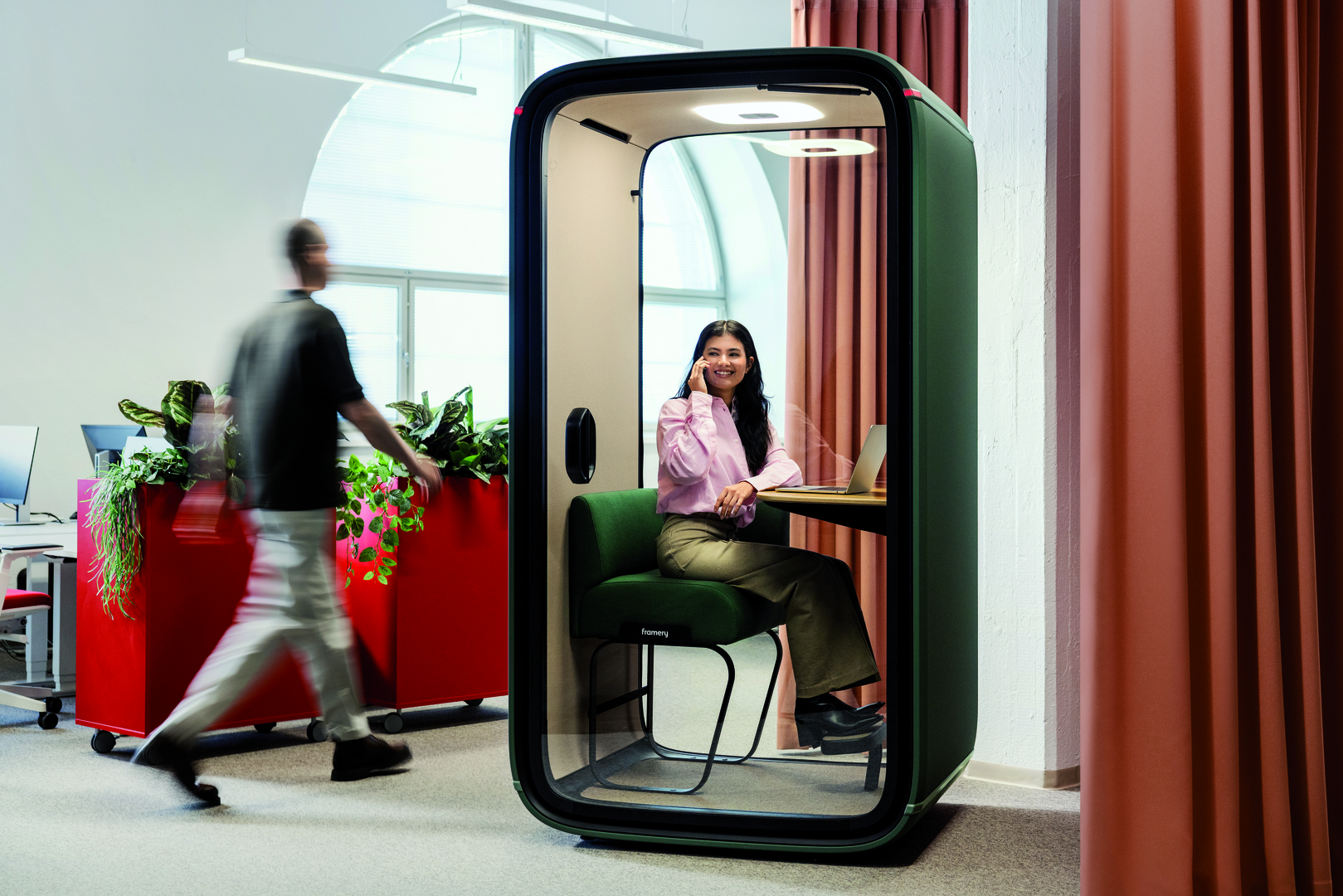 Green office pod with a woman talking on phone, in an open office setting