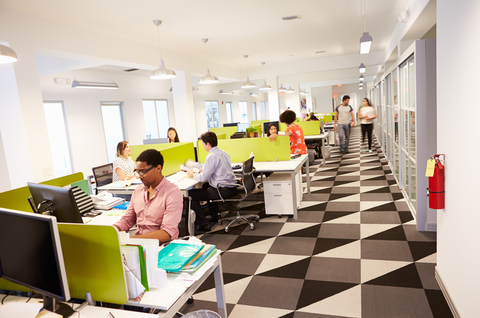 Workers at workstations with yellow privacy panels and patterned black-gray-white floor tiles