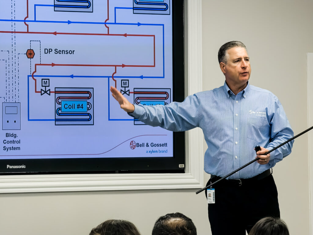 Presenter indicating large screen with building control system diagram during Bell & Gossett Little Red Schoolhouse training program