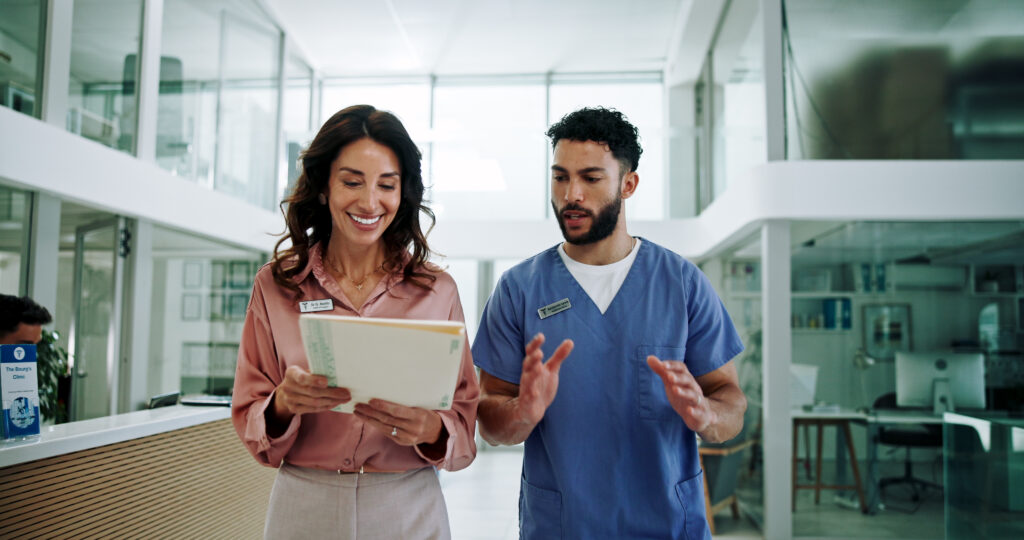 Woman in office attire and man in scrubs in conversation in healthcare setting