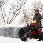 Man drdiving Toro stand-on mower with power broom attachment