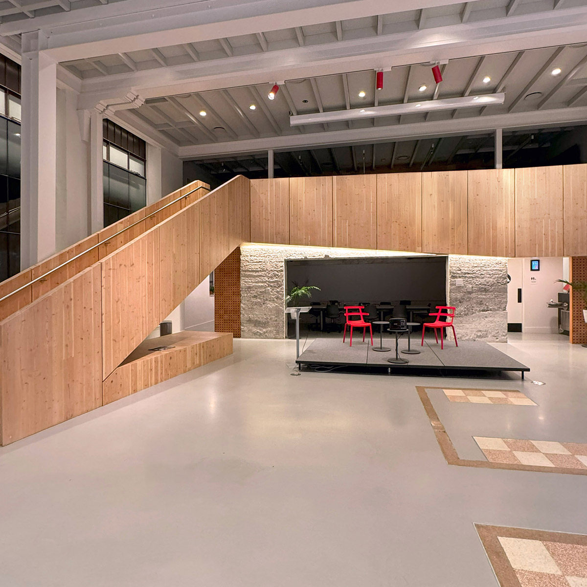 Commercial interior with high beams and wooden staircase, showing lighting design
